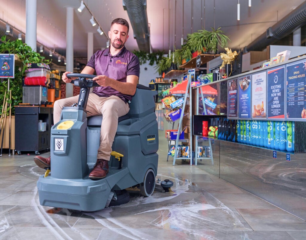 Worker driving ride-on floor cleaning machine inside a retail store maintained by IntiClean