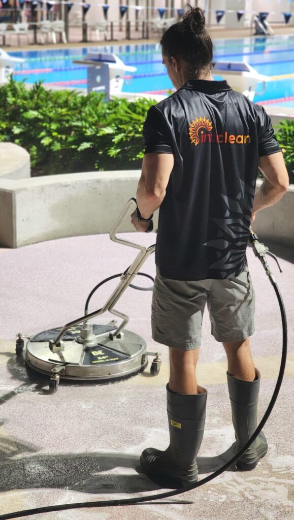 Inticlean worker pressure cleaning poolside pavement area using rotary surface cleaner machine