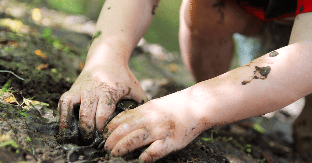 Child with muddy hands outdoors highlighting need for Brisbane Inticlean childcare cleaning services