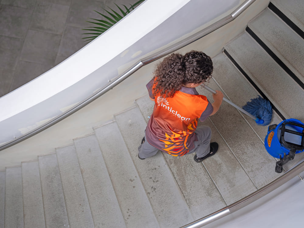 Inticlean staff mopping indoor staircase with bucket and cleaning equipment placed nearby