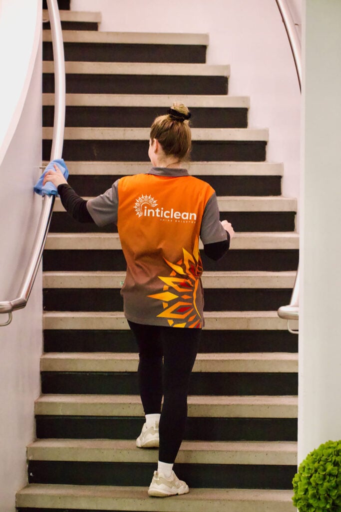 IntiClean worker wiping stair railing with cloth while cleaning indoor staircase area