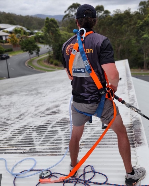 Inticlean worker secured with safety harness preparing roof cleaning on residential property